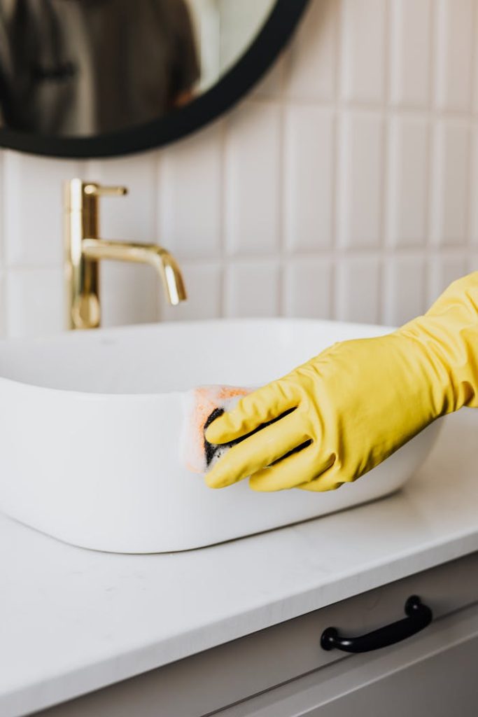 The Art of Drawing Readers In: Your attractive post title goes here Crop faceless person in yellow rubber protective glove wiping surface of white sink in bathroom with sponge and cleaning agent